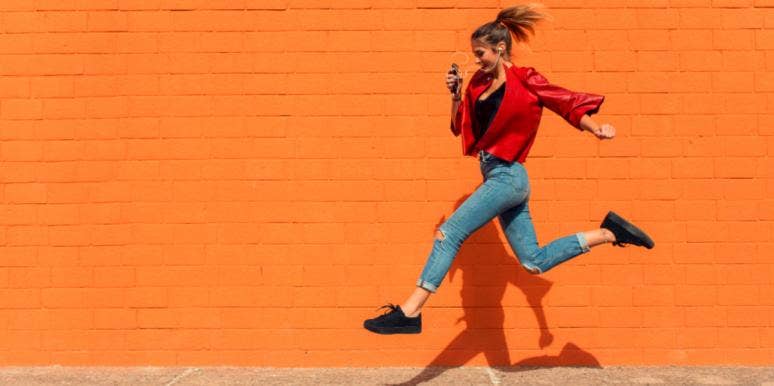 woman jumping over sidewalk crack orange background