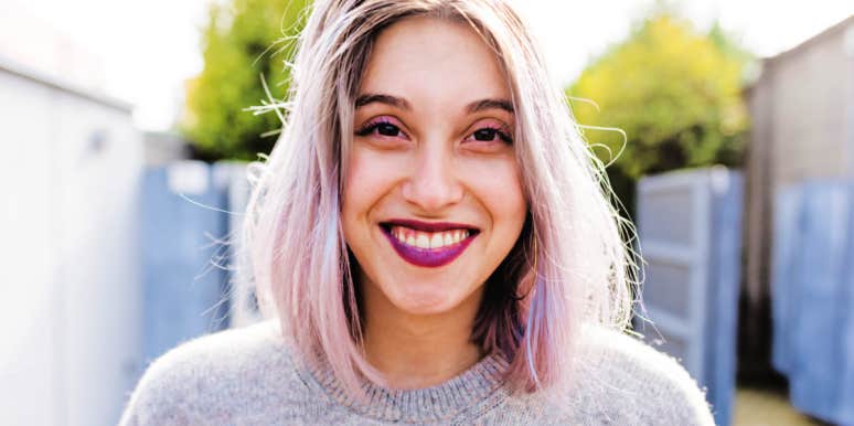 young woman with pink lipstick and brown eyes, white and pink hair, looks at camera smiling