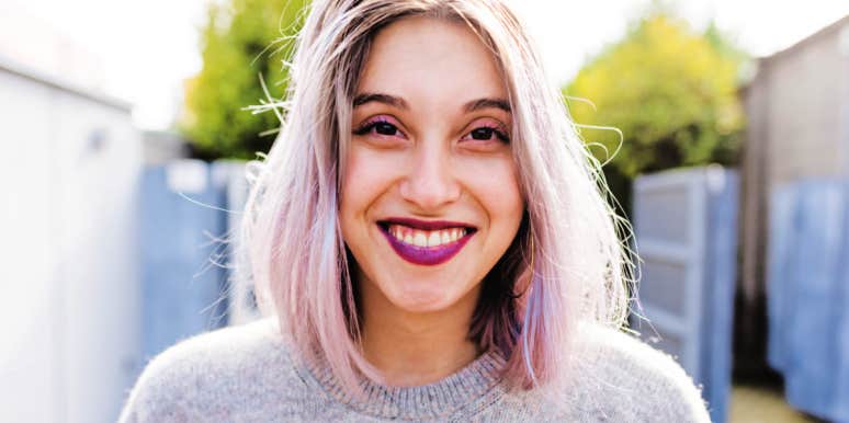 signs you're too hard on yourself young woman with pink lipstick and brown eyes, white and pink hair, looks at camera smiling
