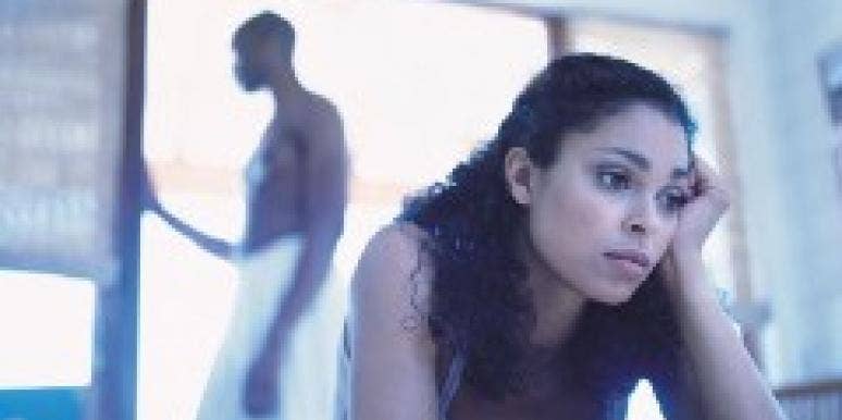 Thinking About Cheating? Read This First. unhappy woman on bed with man in the background