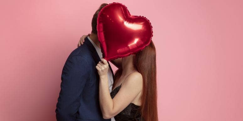 couple kissing behind heart balloon