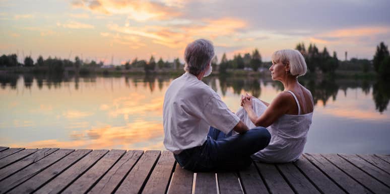 middle-aged couple sitting together on lake bank enjoying beautiful sunset