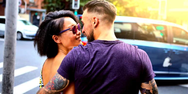man with back to camera embracing woman wearing sunglasses and smiling
