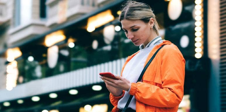 woman typing on her phone in orange jacket
