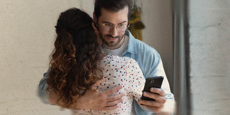 man looking at his phone when hugging a woman