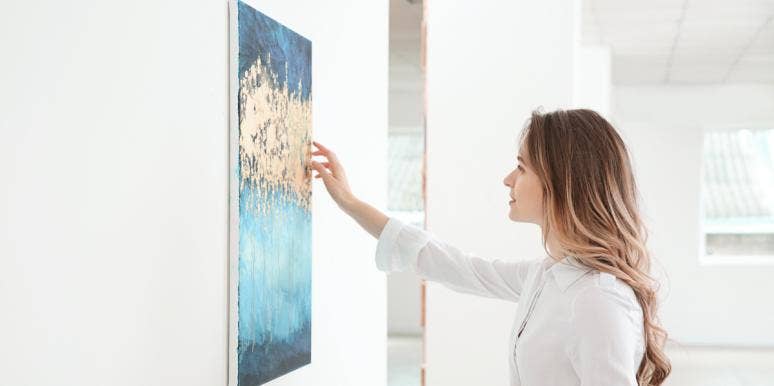 Woman Keeps Dead Sister's Paintings In The House After Marrying Her Husband woman looking at painting hanging on the wall