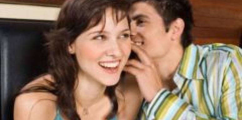 man whispering in woman's ear