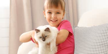 Little girl holding a cat and smiling. 