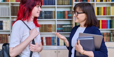Female teacher talking to teenage student girl inside library