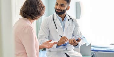  male doctor consulting patient and filling form at consultation