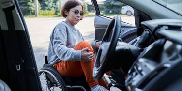 Woman opening door of her car and getting inside from sitting on wheelchair