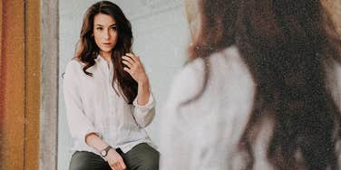 Woman looking in mirror judging herself, biological reason we do so