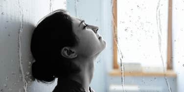 Woman grieving loss, leaning against wall crying 