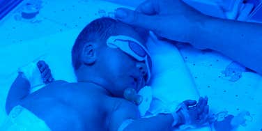Baby in blue light bed, mothers hand touching his head