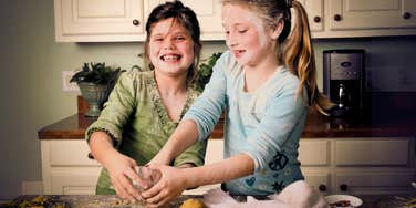 Mother taking hands off 1980's parenting approach while children bake in kitchen making a mess. 
