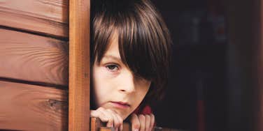Young boy looking out of treehouse window. 