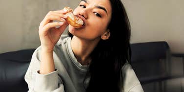 Woman eating a sugary donut at home, contributing to her anxiety. 