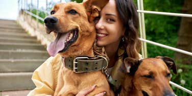 Young charming smiling girl is resting while walking in the park with two golden dogs.
