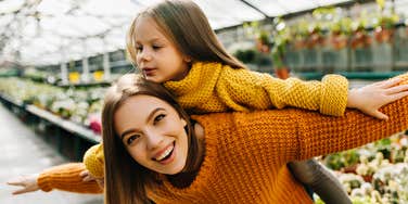 Laughing emotional woman posing in greenhouse with kid