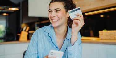 Gen Z woman smiling and holding up a credit card.