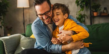 Man smiling and hugging his young son on a couch.