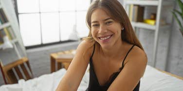 smiling woman sitting in bed about to use adam & eve products