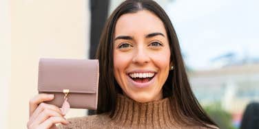frugal woman holding up wallet smiling