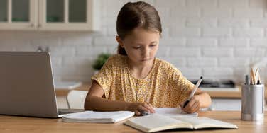 little girl taking exam with laptop and notebook