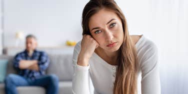 stressed wife looking annoyed while husband sits in background lazily
