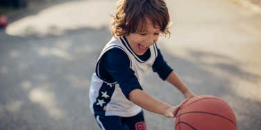 Boy playing basketball in driveway after neighbor sues family over hoop