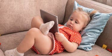 Little girl under 2 using a screen while lying on the couch