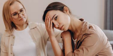 upset woman sitting next to mother who makes her feel like a failure