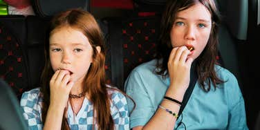 Kids selfishly upset eating snacks in the back of the car during road trip. 