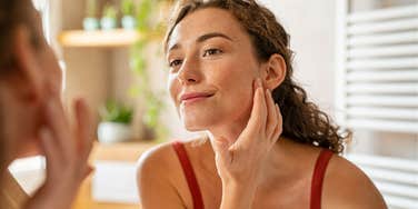 woman with unsanitary habits touching face in mirror
