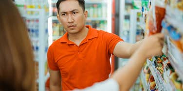 frugal man annoyed with womans purchase at grocery store