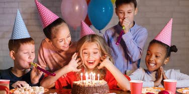 girl blowing out candles on cake at birthday party