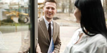 woman holding door open for man who is looking at her smiling