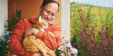 older man holding pet cat standing outside
