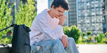 upset young man sitting on park bench outside