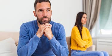 unhappy man sitting next to lazy wife on couch