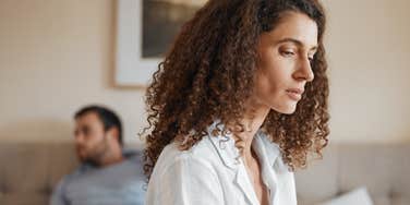 upset woman sitting on edge of bed away from partner