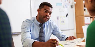 serious male teacher talking to students in classroom