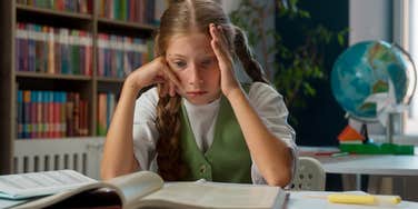 anxious little girl sitting in classroom looking at textbook