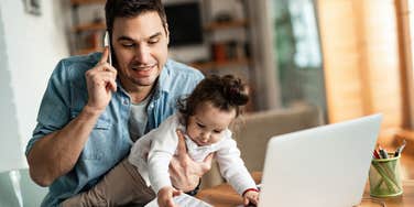 dad working on laptop and holding infant daughter