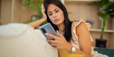 sad woman looking at phone sitting on couch at home