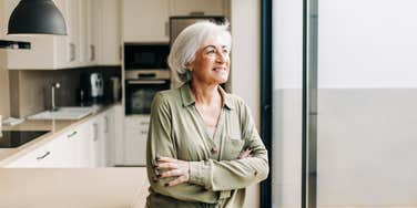 older woman standing in kitchen looking out window