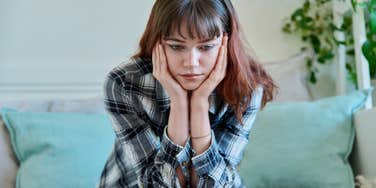 upset woman sitting on couch holding head in hands