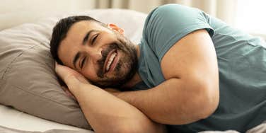 happy smiling man laying in bed after sleeping alone