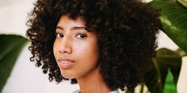Positive Black woman with curly hair near green plants, confident and respected, showing subtle signs of true respect.