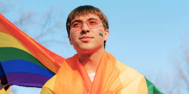 Teen boy wearing an LGBTQ pride flag wrapped around his shoulders, representing efforts to stop anti-LGBTQ bullying